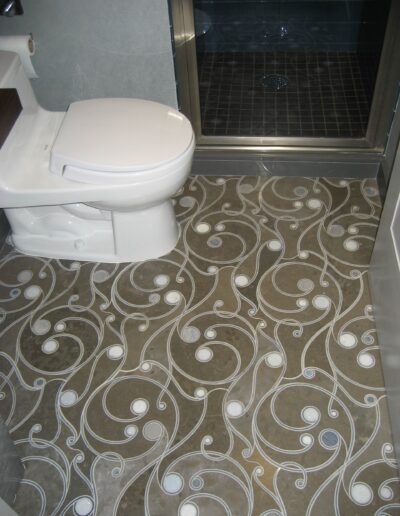 A bathroom with a decorative tile floor, featuring a white toilet next to a glass-door shower.