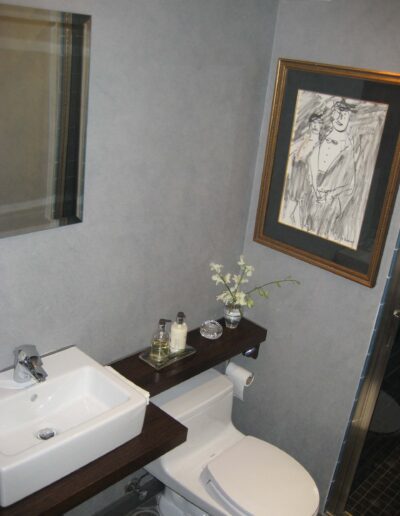 A modern bathroom with a white sink and toilet, complemented by a framed artwork on the wall and decorative flowers on the countertop.