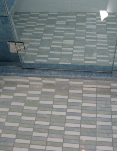 Modern bathroom with glass shower enclosure and tiled flooring in shades of blue and white.