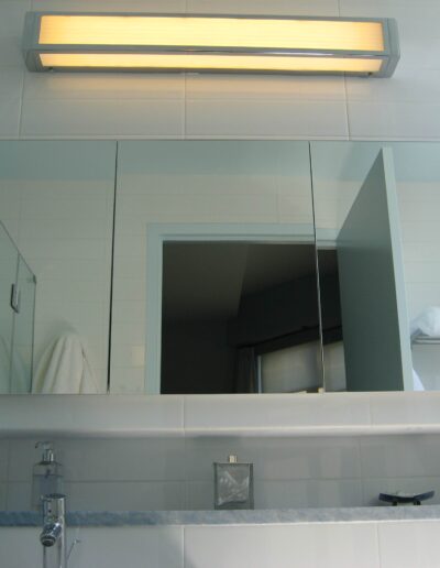 A modern bathroom mirror with reflection of interior, featuring a wall-mounted light fixture above.