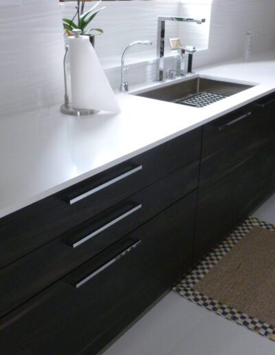 Modern kitchen with dark cabinetry and white countertops, featuring a sink and decorative elements.