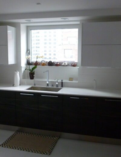 Modern kitchen with white countertops, dark cabinetry, and a window overlooking a building.