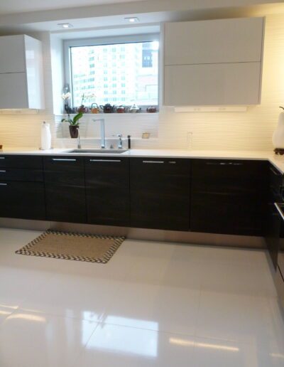 Modern kitchen interior with black cabinetry and white countertops, featuring a view of the cityscape through the window.