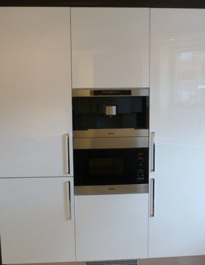 Modern kitchen with built-in stainless steel oven and microwave within white cabinetry.