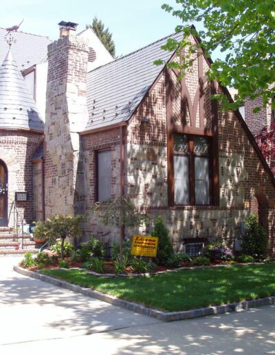 Tudor-style suburban house with a well-maintained front yard and parked cars.