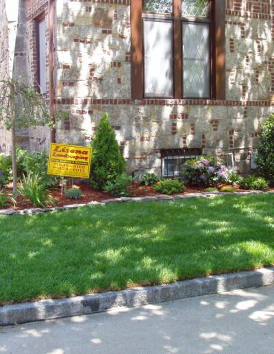 Brick house with large windows and a "for sale" sign in the front lawn.