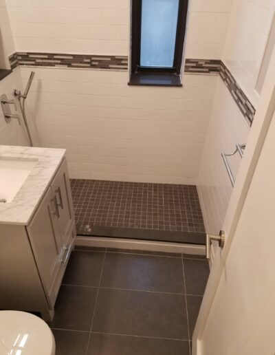 A modern bathroom with beige walls, dark tiled flooring, and a white sink vanity.