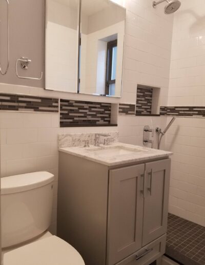 Modern bathroom interior with white and gray color scheme, featuring a vanity with a marble countertop, mirror, and a subway tile wall.