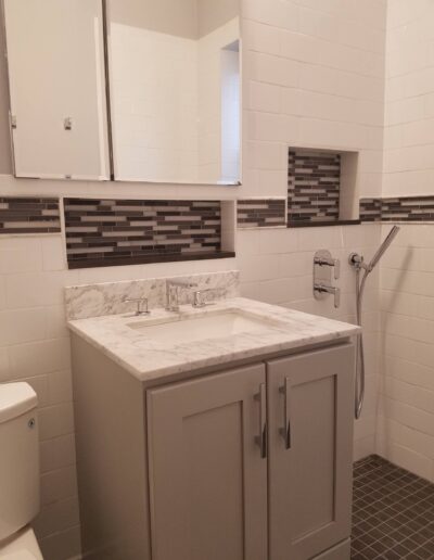 A modern bathroom interior with gray cabinetry, marble countertop, and white subway tiles.