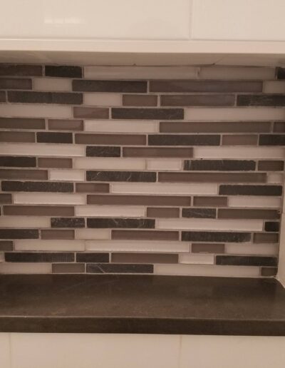 A built-in shower niche with white and gray tiled walls and shelving.