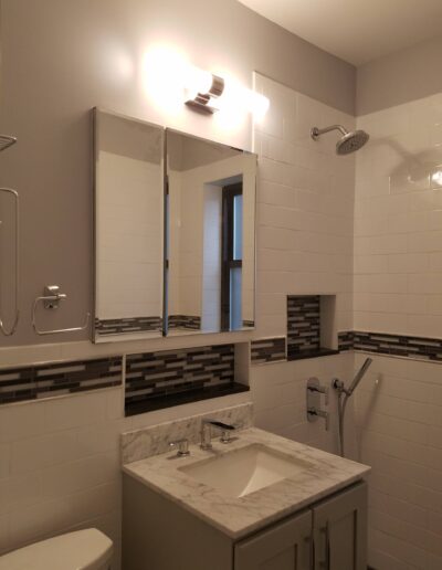 Modern bathroom interior with white tile walls, vanity with marble countertop, and mirrored medicine cabinet.