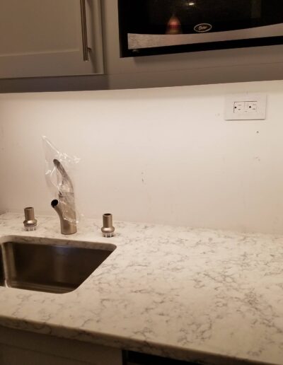 A modern kitchen countertop with a sink and faucet, with a white tiled backsplash and under-cabinet lighting.