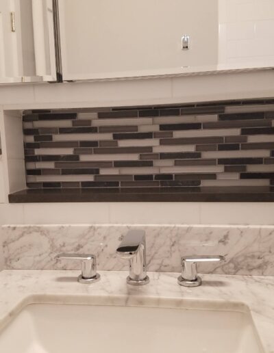 A modern bathroom sink with marble countertop and mosaic backsplash.