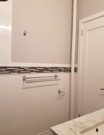 Modern bathroom interior with white subway tiles, decorative border, marble countertop, and towel rack.