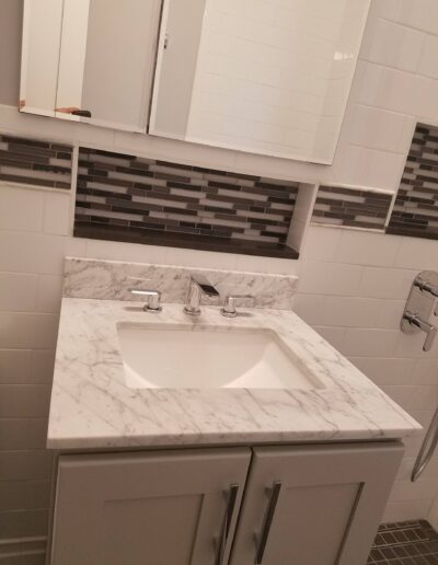 Modern bathroom with white cabinets, marble countertop, and a mosaic backsplash.