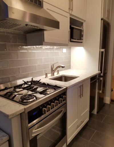 Modern kitchen interior with stainless steel appliances, gray cabinetry, and marble countertops.