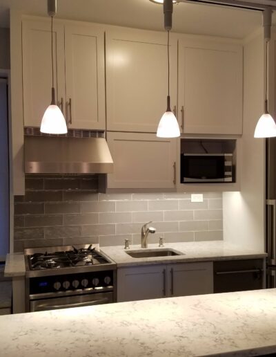 Modern kitchen interior with stainless steel appliances, white cabinetry, and pendant lighting.