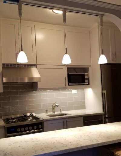 A modern kitchen with white cabinetry, stainless steel appliances, and pendant lighting over a marble countertop.