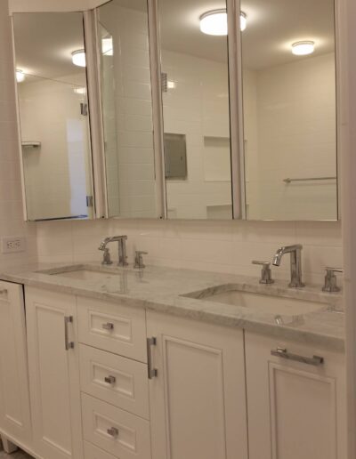 A clean and modern bathroom vanity with white cabinets, marble countertop, and a triple mirror setup.