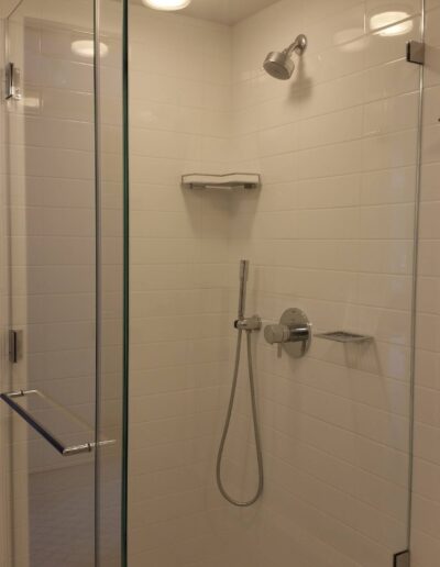 Modern bathroom with a glass-enclosed shower, white subway tiles, and stainless steel fixtures.