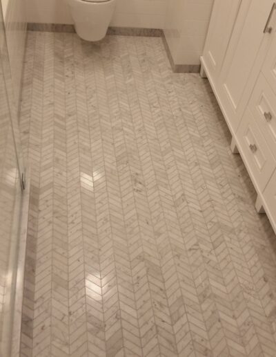 Modern bathroom with white cabinetry and herringbone tile flooring.