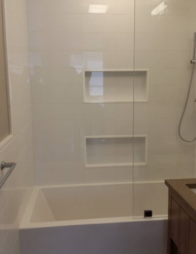 A modern bathroom with a white bathtub and a glass shower partition.