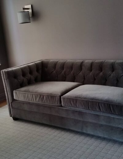 A gray tufted sofa in a room with gray walls and a large window.