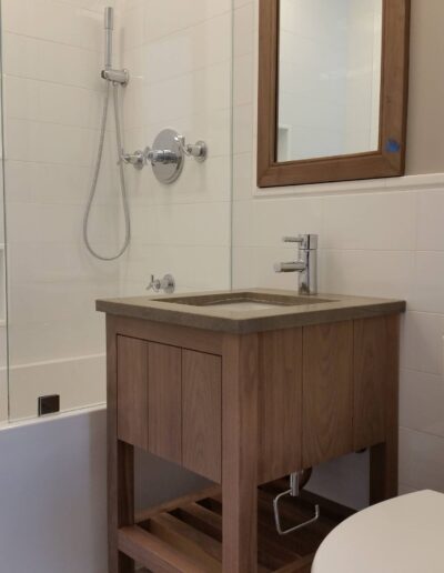 Modern bathroom interior featuring a wooden vanity with a basin, a toilet, and a glass-enclosed shower area.