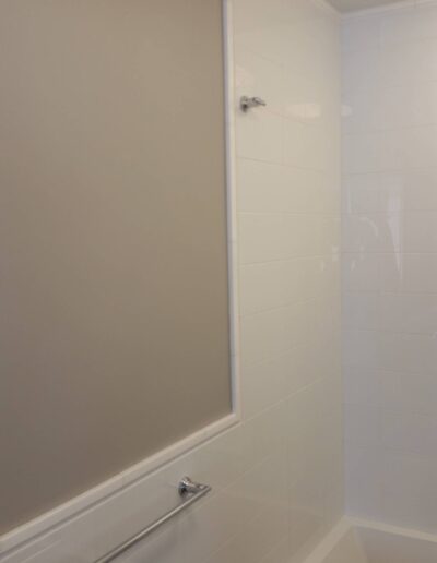 A modern bathroom with a white tiled shower area and a tan wall.