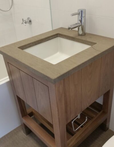 Modern bathroom vanity with an undermount sink and a single faucet, featuring a wooden cabinet and stone countertop.