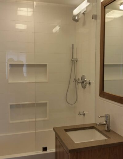 Modern bathroom with a walk-in shower, white tiles, and a wooden vanity.