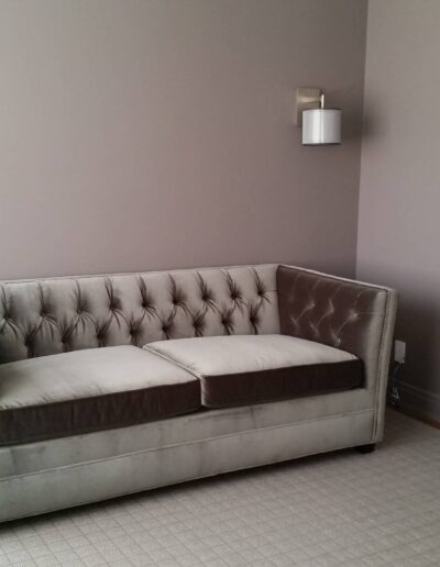 A gray tufted sofa against a gray wall with two wall sconces on either side.