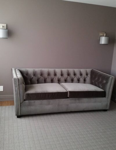 Gray tufted sofa against a gray wall with two wall-mounted lamps.