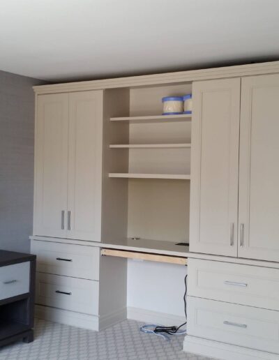 Modern home office with built-in beige cabinetry and a gray desk against a textured wallpaper.