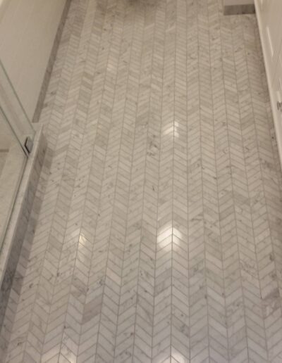 A bathroom with white textured floor tiles, featuring a glass shower door and a white toilet.